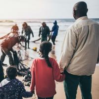 		Man with children watching others pulling nets in from the sea
	