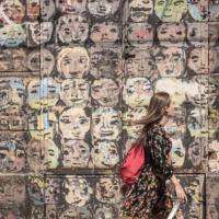		Person walking past a wall painted with many faces
	