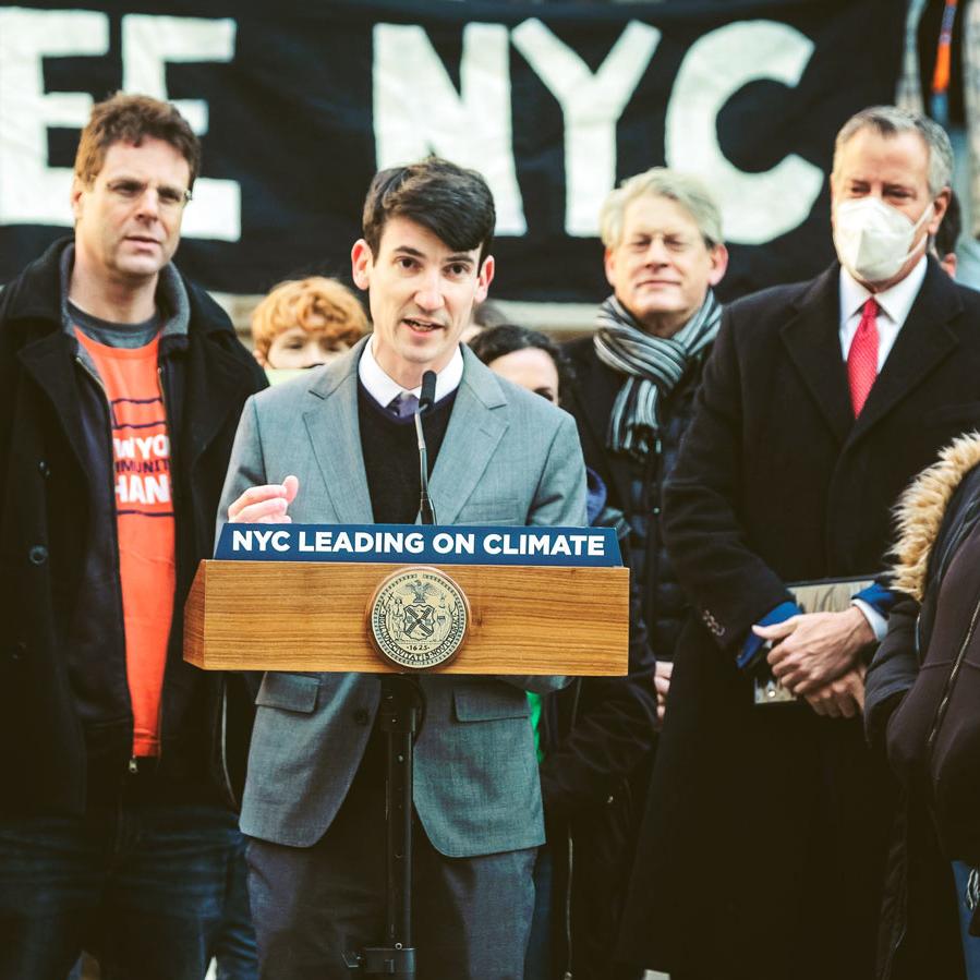 		Person wearing gray suit speaks at a podium that says &#039;NYC LEADING ON CLIMATE&#039;
	