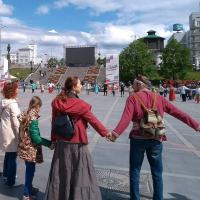 		People in a town square hold hands in a large circle
	