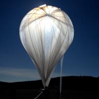 		Light shines through gossamer fabric of a large, inflated balloon against a dark sky
	