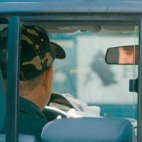 		Person in the driver&#039;s seat of a pickup truck, seen through the back window
	