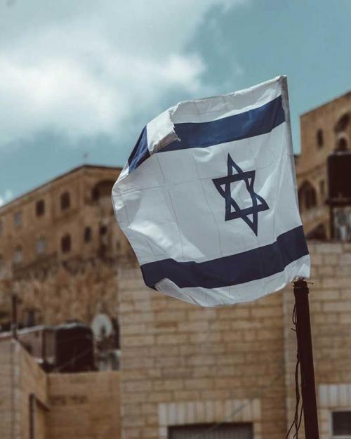		White and blue Israeli flag in front of stone buildings
	