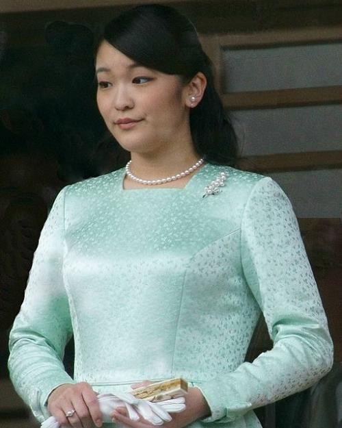 		Princess Mako wearing pearl earrings, necklace and pin, and a long sleeved green dress; she is holding white gloves and a fan. 
	