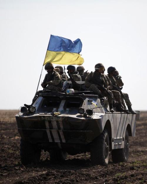 		armored vehicle flying a blue and yellow flage
	