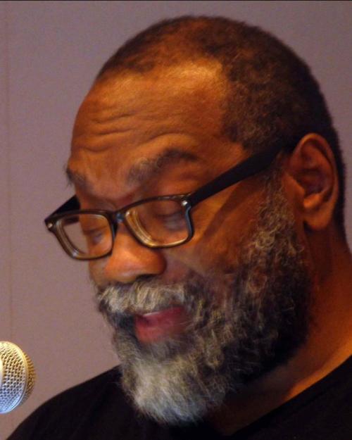 		Fred Moten, with a mostly white beard and black glasses in front of a microphone
	