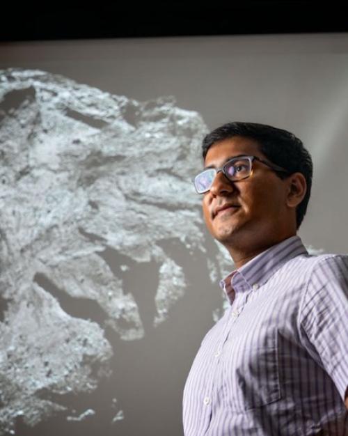 		Person standing in front of a huge black &amp;amp; white image of a comet with a rocky surface
	
