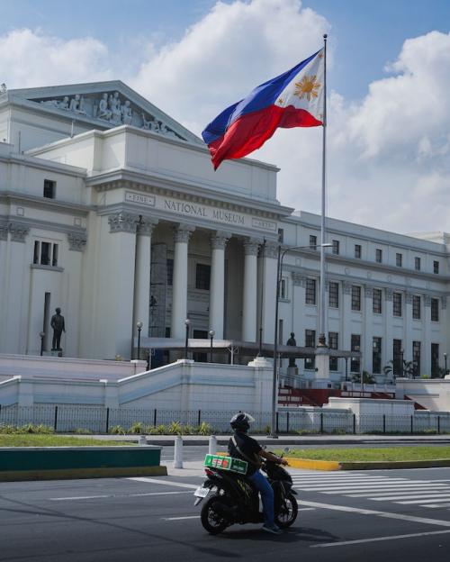 		Motorcycle drives past a stone &quot;National Museum&quot; fronted by the Philippine flag
	