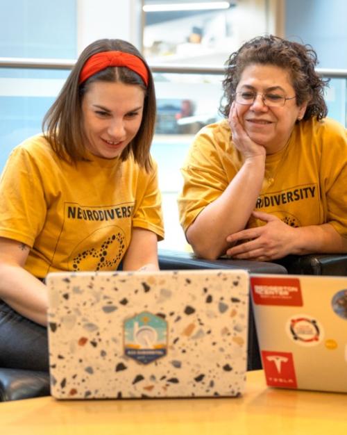		Three people wearing matching yellow t-shirts look at two laptop computers
	