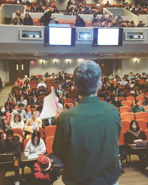 		Person stands in front of a mostly full auditorium
	