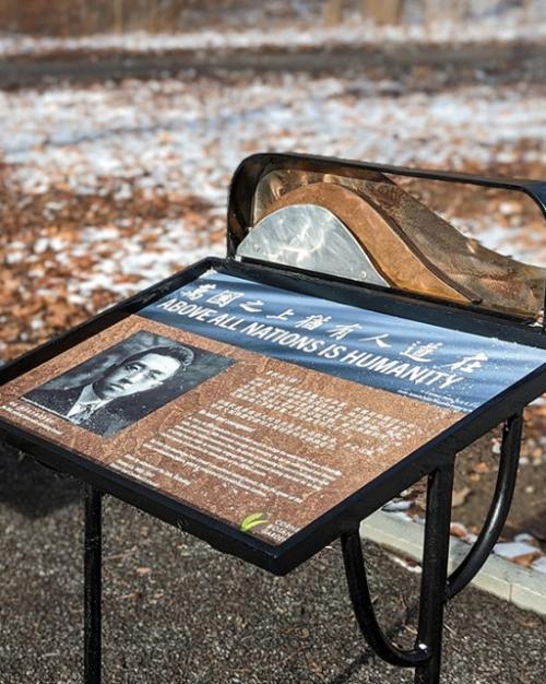 		In a natural areas, a stone bench is next to an interpretive sign
	