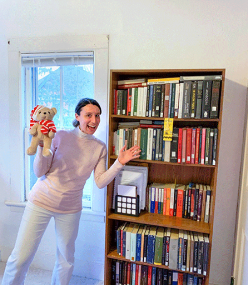		 A graduate student smiles in front of all her books
	
