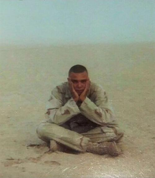 		 Marine soldier sitting cross-legged in the desert.
	