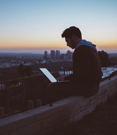  Person looking at a laptop while sitting on a rooftop at sunset