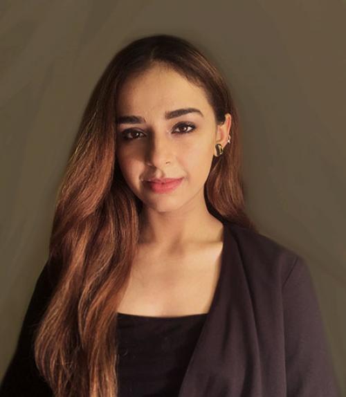  Headshot of a young woman in dress clothes with long hair in front of a gray backdrop.