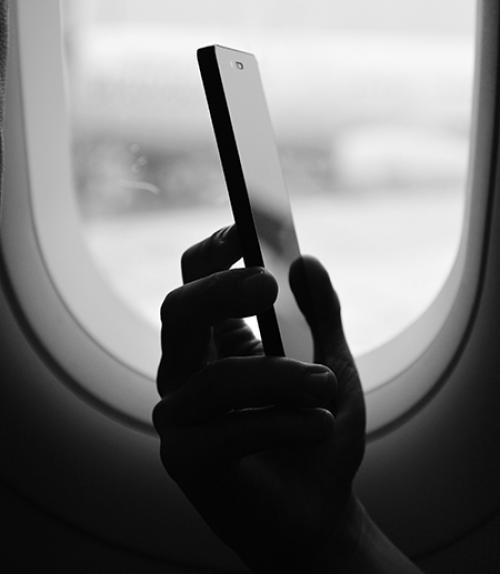 		 hand holding a cell phone frame by an airplane window
	