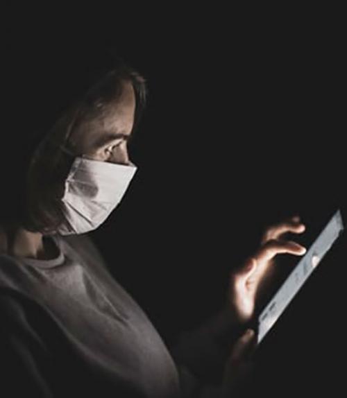 		 A woman wearing a mask using a touchscreen
	