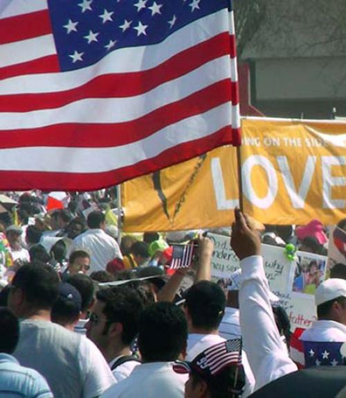 		 Image of a rally with an American flag and a sign saying &amp;quot;love&amp;quot;
	