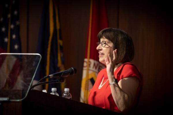 Person wearing red and pearls, speaking at a podium