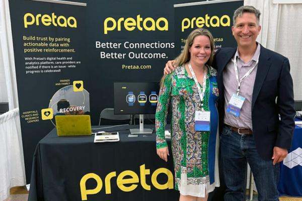 Two people stand in front of a display table for the product Pretaa