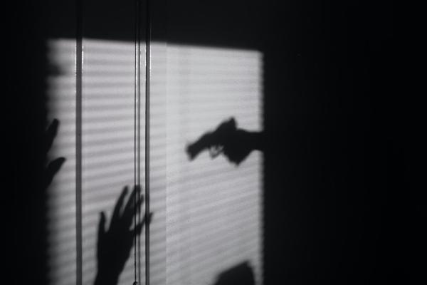 Silhouettes on a wall show a gun aimed at two hands held up in surrender; a scene of nighttime crime