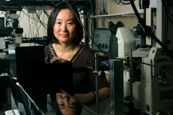 Michelle Wang, next to a microscope and with dangling wires and equipment behind her
