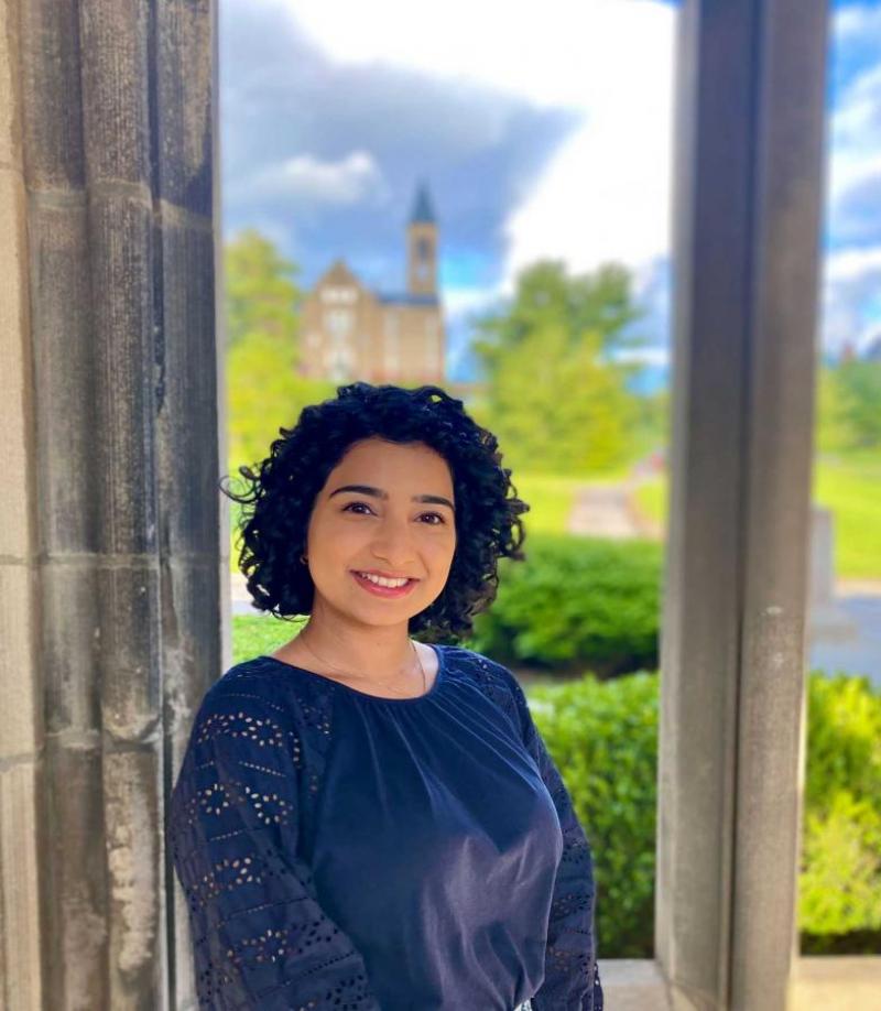 Kamla Arshad ’21 in a blue blouse with the clocktower in the background.