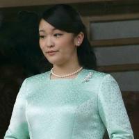 Princess Mako wearing pearl earrings, necklace and pin, and a long sleeved green dress; she is holding white gloves and a fan. 