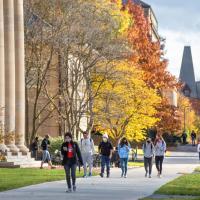 Students walking in front of Goldwin Smith Hall, with trees showing Autumn colors