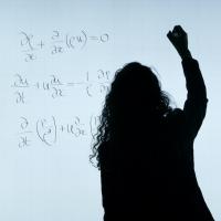 Person silhouetted against a white background, writing equations on a board