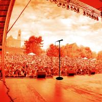 Red-tinted image of a stage from the performers point of view, looking out at a large crowd outside