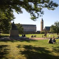 Several people sit on a shadowed lawn between university buildings