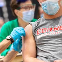 Medical professoional wearing a mask and protective gloves gives a shot to a person wearing a Cornell Big Red t-shirt