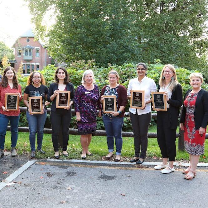 Nine people stand in a line; six of them hold plaques