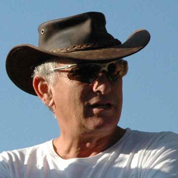 White-haired Aviam wearing a leather cowboy hat, wearing sunglasses and a white t-shirt.