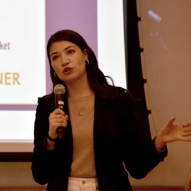 Person speaks with a microphone in front of a screen