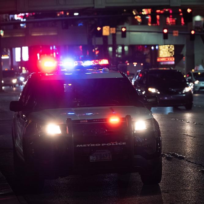 A police vehicle at night, red and blue lights reflecting off wet pavement