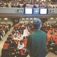 		Person stands in front of a mostly full auditorium
	