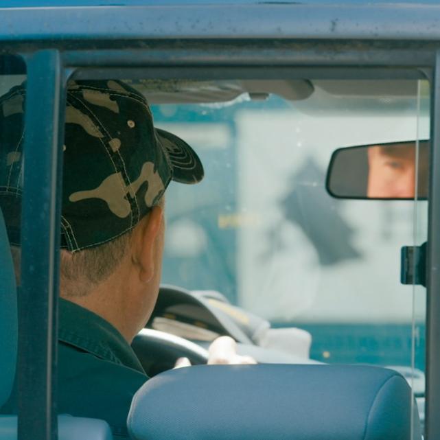 Person in the driver's seat of a pickup truck, seen through the back window