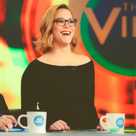 		Two people appearing on a TV talk show, sitting at a desk with mugs in front of them
	