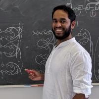 		Darren Pereira in a white shirt rolled up to his elbows, smiling with a black beard and mustache, standing at chalkboard in front of diagrams.
	