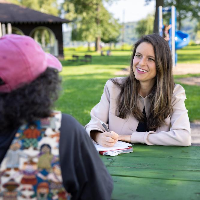 Two people sitting at a table, conversing in a shady area of a park