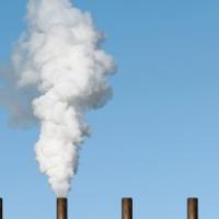 		five smoke stacks against a blue sky; the second from left belches smoke
	