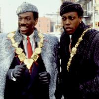 Two people -- characters in a film -- wearing large coats and gold jewelry