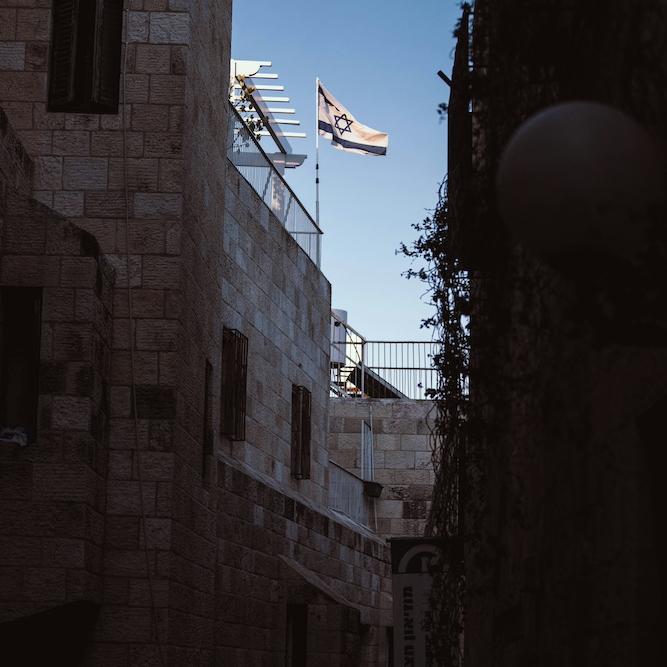 White and blue flag of Israel seen at a distance between two buildings