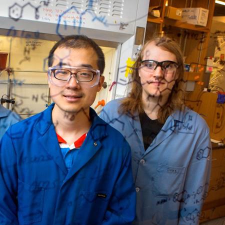		Two professors in lab coats looking at chemistry writing on a white board
	