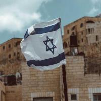 White and blue Israeli flag in front of stone buildings