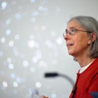 Martha Haynes with glasses, shoulder-length gray hair in a red top, with blurred stars on screen behind her
