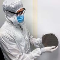 Person in white laboratory clean suit holds up a black disk
