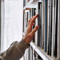 A hand reaching for a book on a bookshelf